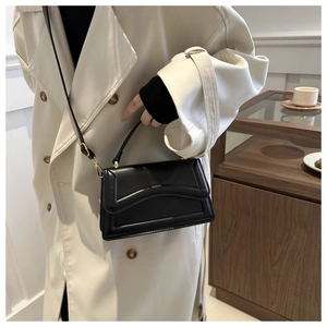 Side view of black crossbody bag with wavy stitching and gold hardware on model