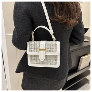 Details einer weißen Tweed-Handtasche mit goldener Schnalle auf einem grauen Mantel