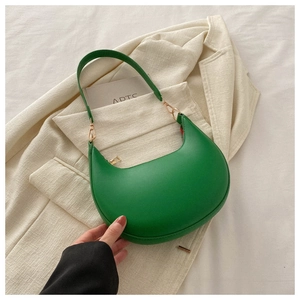 Detail view of green crescent underarm bag with gold zipper on a beige suit