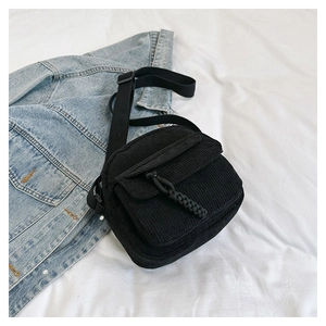 Stylish black corduroy crossbody bag with front pocket shown on white fabric and denim jacket
