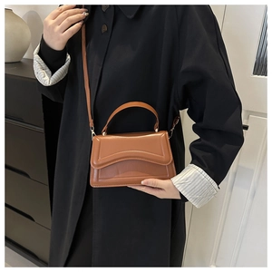 Brown leather handbag with unique wave stitching worn by a model in a minimalist setting