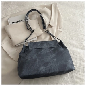 Detail of grey washed canvas shoulder bag with silver chain strap on beige fabric background