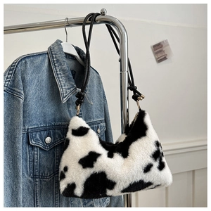 Detail of plush cow print underarm bag with black leather strap on denim jacket