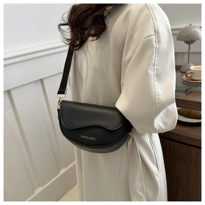 Détail du sac selle noir avec lettrage doré et bandoulière en tissu rayé bicolore