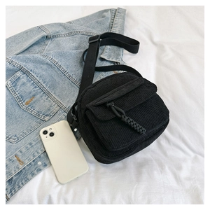 Detailed texture of black corduroy fabric on a minimalist crossbody bag with woven drawstring