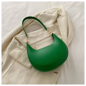 Detail of green hobo bag with smooth leather finish and gold zipper on beige blazer