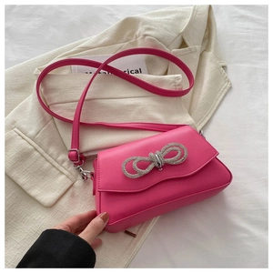 Detail of rose red leather crossbody bag with sparkling rhinestone bow on textured fabric