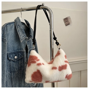 Pink and white cow print plush shoulder bag with black rope strap on clothes hanger