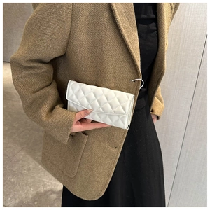 Close-up of a white quilted leather clutch bag held by a model in a tweed coat