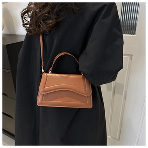 Brown leather handbag with wavy flap and stitching detail worn with a black coat