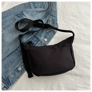Detail of a black minimalist nylon crossbody bag with adjustable wide strap on denim