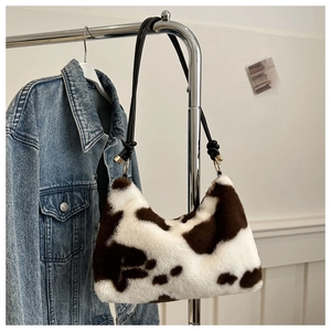 Detail of plush cow print shoulder bag with black leather strap and gold ring accents