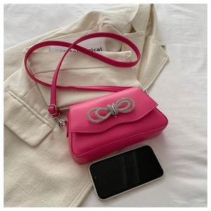 Detail of fuchsia square bag featuring a crystal bow and smooth synthetic leather texture
