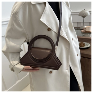 Deep brown geometric handbag with circular handle and slender strap in a lifestyle setting