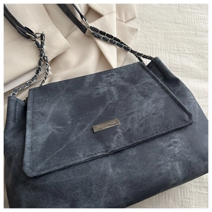 Detail of grey denim texture and metal logo plaque on a stylish crossbody chain bag