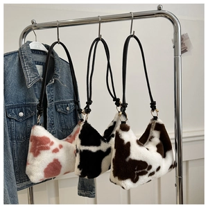 Plush shoulder bags with cow patterns in pink, black, and brown hanging on a metal rack