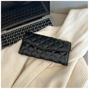 Detail of black quilted leather clutch bag on beige knitwear with laptop background