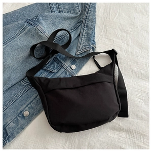 Detail view of a black nylon crossbody bag paired with a blue denim jacket on white background