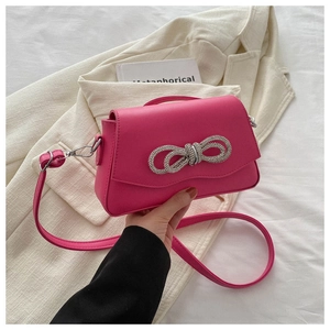 Close-up of fuchsia mini square bag with glittering rhinestone bow and leather strap