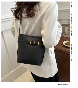 Detail of minimalist black PU bucket bag with gold buckle on a model in white blazer