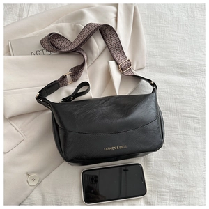 Detail of black pebbled PU leather bag with wide jacquard strap and gold fashion logo