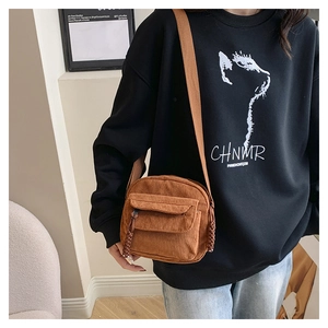 Brown corduroy shoulder bag with braided zipper detail and flap pocket worn by a model