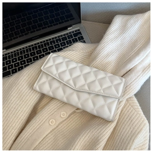 Close-up of a white quilted leather envelope clutch bag on a beige knit sweater