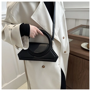 Detail of a black geometric leather handbag featuring a unique circular metal handle and matte finish