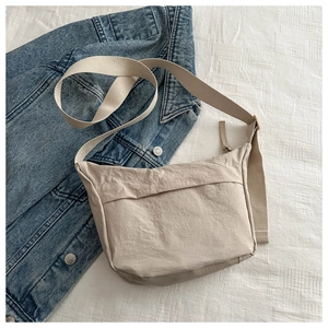 Detail of beige nylon crossbody bag with layered pockets on denim jacket background