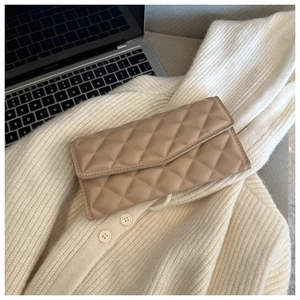 Close-up of beige quilted leather clutch bag with V-shaped flap on a white knit sweater