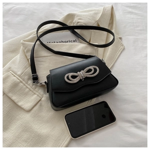 Detail of compact black PU bag with rhinestone bow decoration and phone for scale