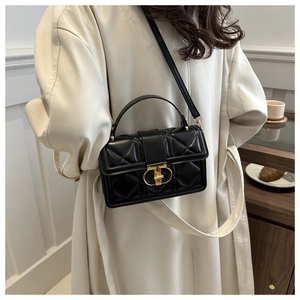 Detail of black quilted leather shoulder bag with a gold ring buckle on a beige coat