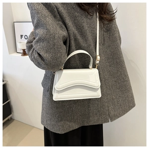 White minimalist crossbody bag with wavy embossed detail worn over a grey blazer