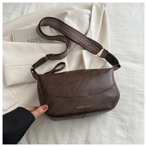 Detailed macro of dark brown saddle bag with gold logo and woven strap on white background