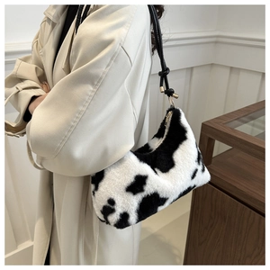 Close-up of cow print plush shoulder bag with black knotted strap and gold zipper