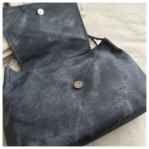 Detail view of washed denim bag featuring silver magnetic buckle and chain strap