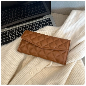Detailed close-up of dark brown quilted leather clutch bag on a white sweater background