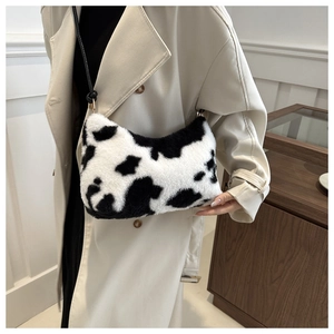 Detailed view of plush cow print shoulder bag with black strap on a beige trench coat