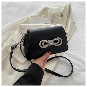 Close-up of black leather crossbody bag featuring a sparkling rhinestone bow detail