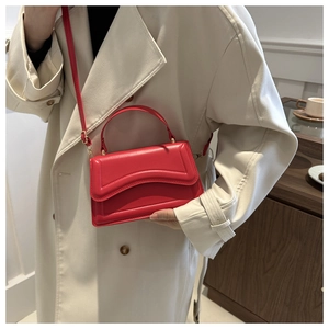 Detail of red glossy leather handbag with wave stitching styled with a beige trench coat