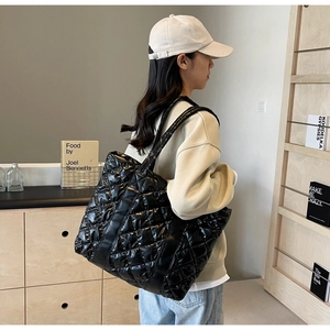Detail of black glossy quilted tote bag with diamond stitching pattern shown on shoulder