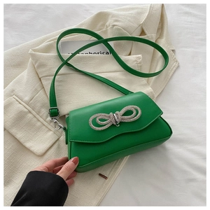 Close-up of green crossbody bag with a large rhinestone bow and flap closure