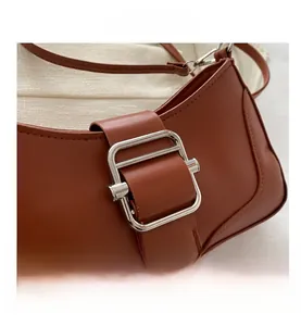Gros plan sur un sac bandoulière en cuir marron avec une grande boucle métallique carrée