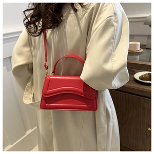 Close-up of a bright red matte leather handbag styled with a cream trench coat