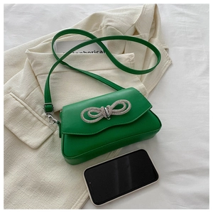 Detail view of green leather crossbody bag with a large sparkling rhinestone bow buckle