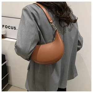 Brown leather crescent shoulder bag styled on a model wearing a grey blazer jacket