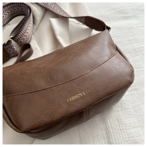 Close-up of brown PU leather bag with gold fashion text and woven jacquard strap