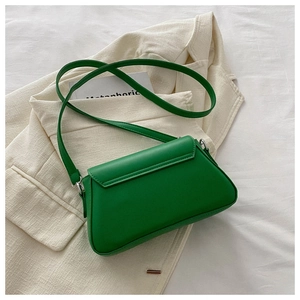 Top view of a bright green mini leather crossbody bag with flap on a white bed sheet