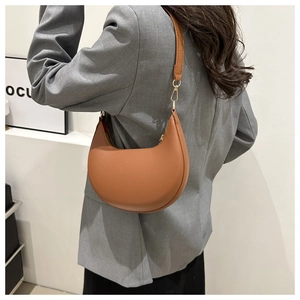 Minimalist brown crescent leather shoulder bag with sleek gold hardware on a model