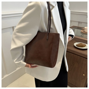 Detail of dark brown faux leather tote bag with slim straps worn by a professional model